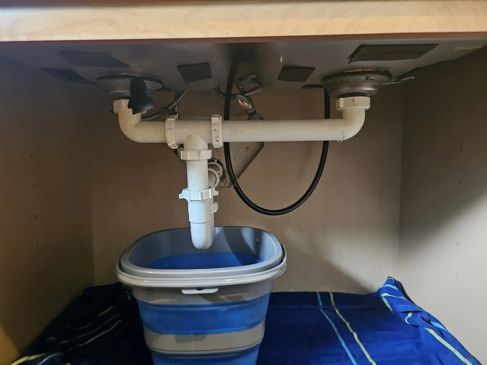 Before: leaking kitchen sink drain with a bucket catching water under the cabinet