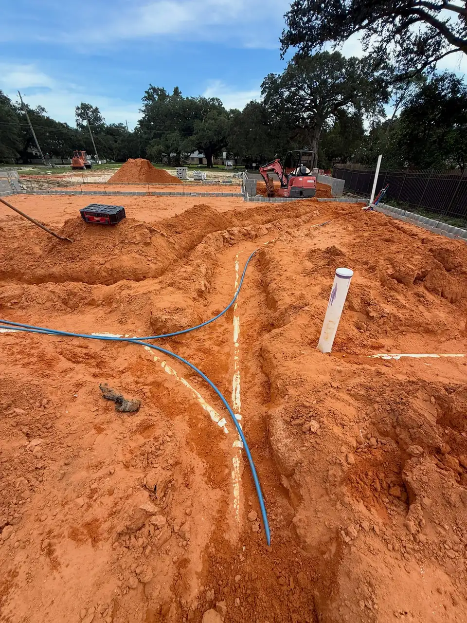 Blue and red PEX supply lines and white PVC drains laid in red clay on a new home site